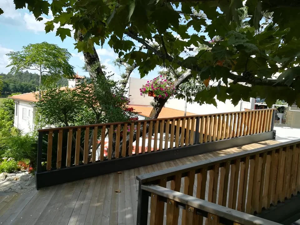 Passagem exterior com guardas de madeira e sombra de árvores